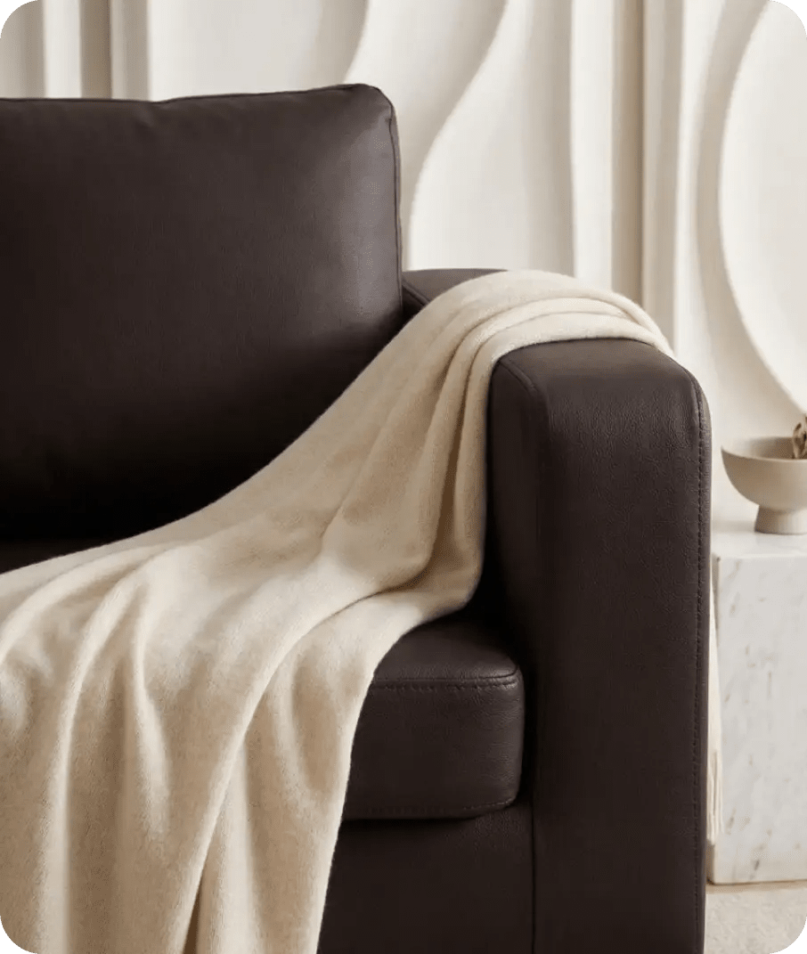 Beige blanket draped over a brown armchair in a minimalistic room.