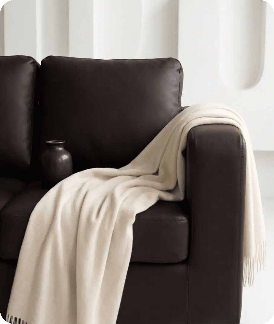 Brown leather sofa with a beige blanket draped over it against a white background
