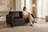 Woman sitting on a brown leather sofa in a modern living room.