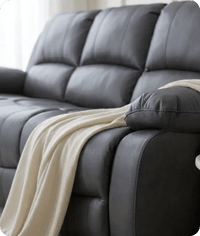 Gray leather sofa with a beige blanket draped over it, set against a neutral background.