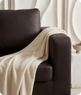 Beige blanket draped over a brown armchair in a minimalistic room.