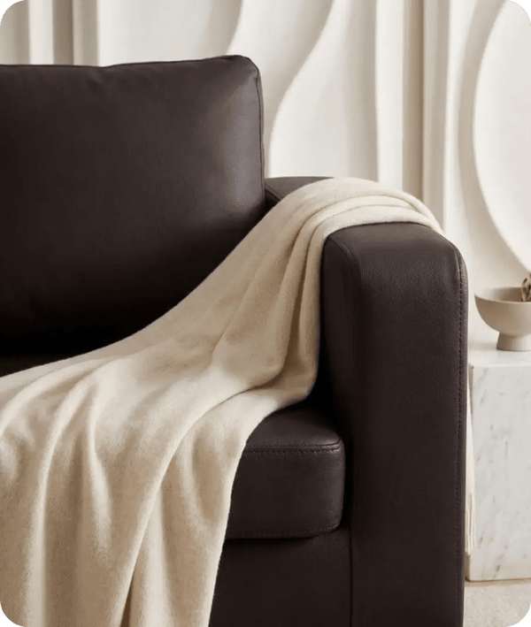 Beige blanket draped over a brown armchair in a minimalistic room.