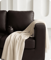 Brown leather sofa with a beige blanket draped over it against a white background