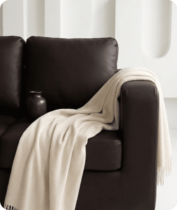 Brown leather sofa with a beige blanket draped over it against a white background